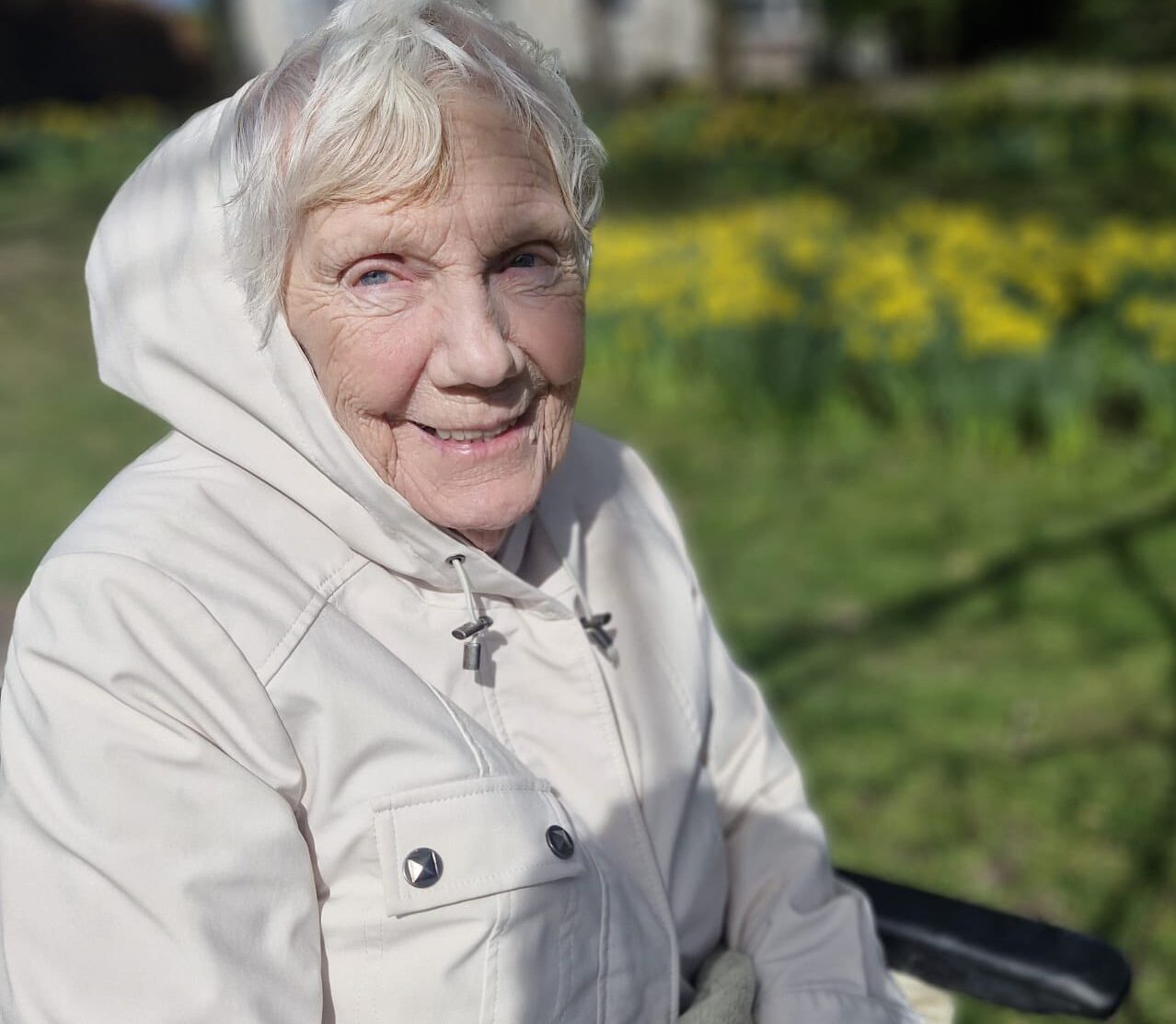 older lady wearing a white hooded jacket smiling at the camera