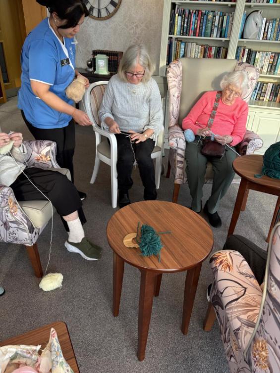 older ladies knitting with a carer next to them